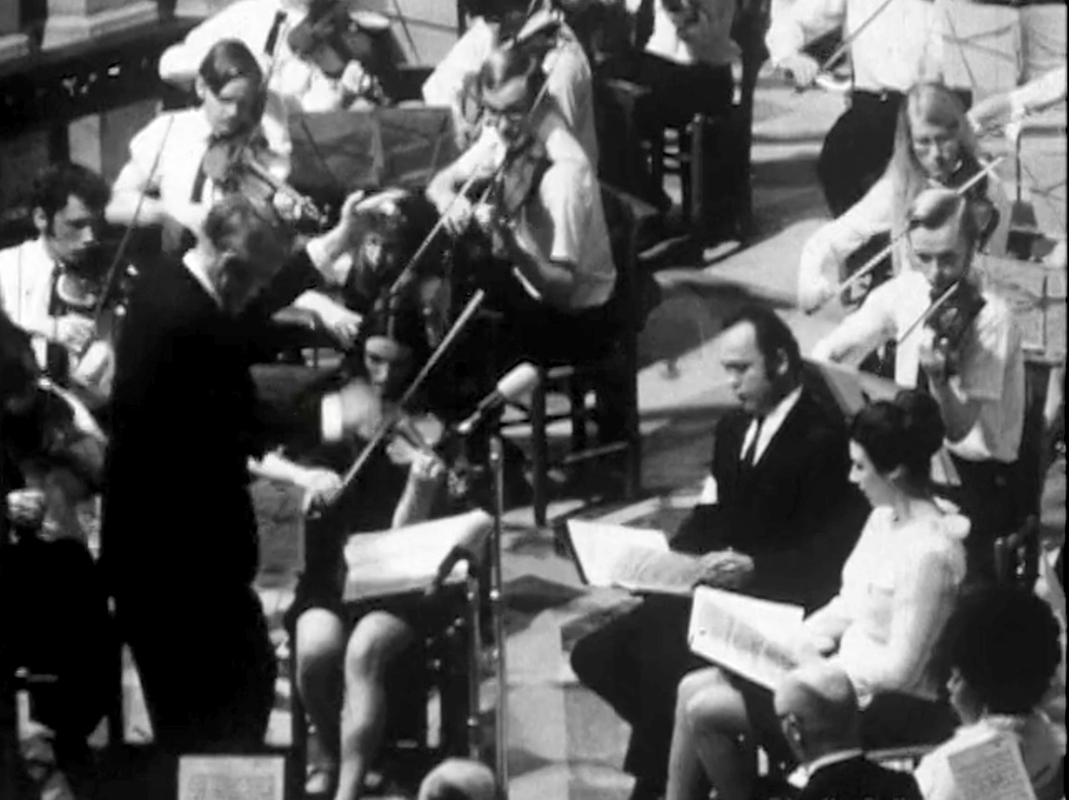 Two soloists are seated in front of the conductor, by the violin section.