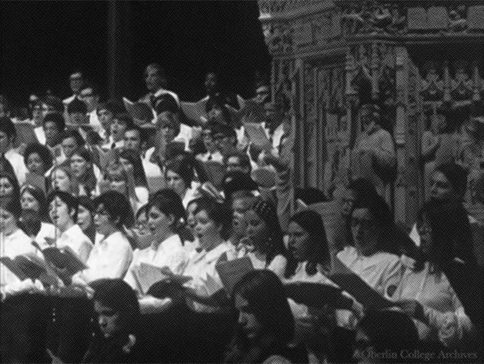 A choir of young women and men perform in the cathedral. In the background are statues of religious figures.
